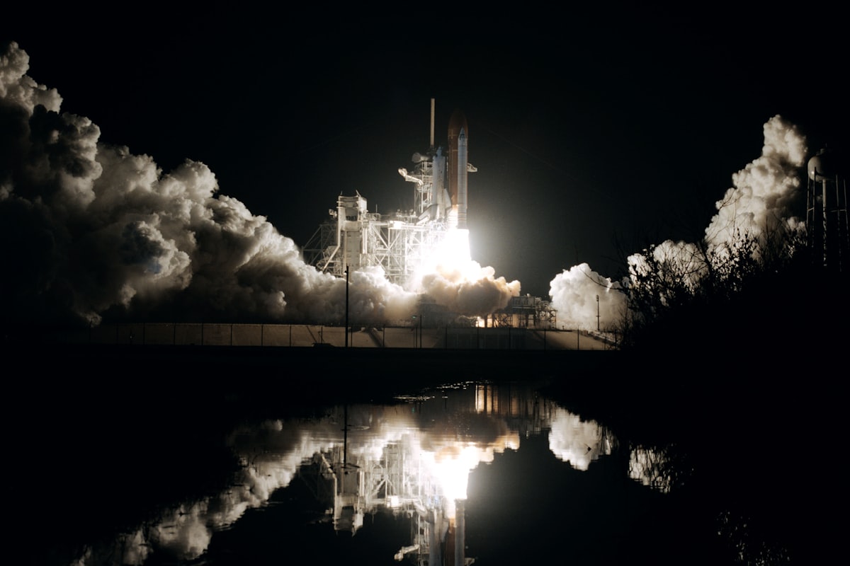 Space shuttle launching at night, its light reflected in nearby water